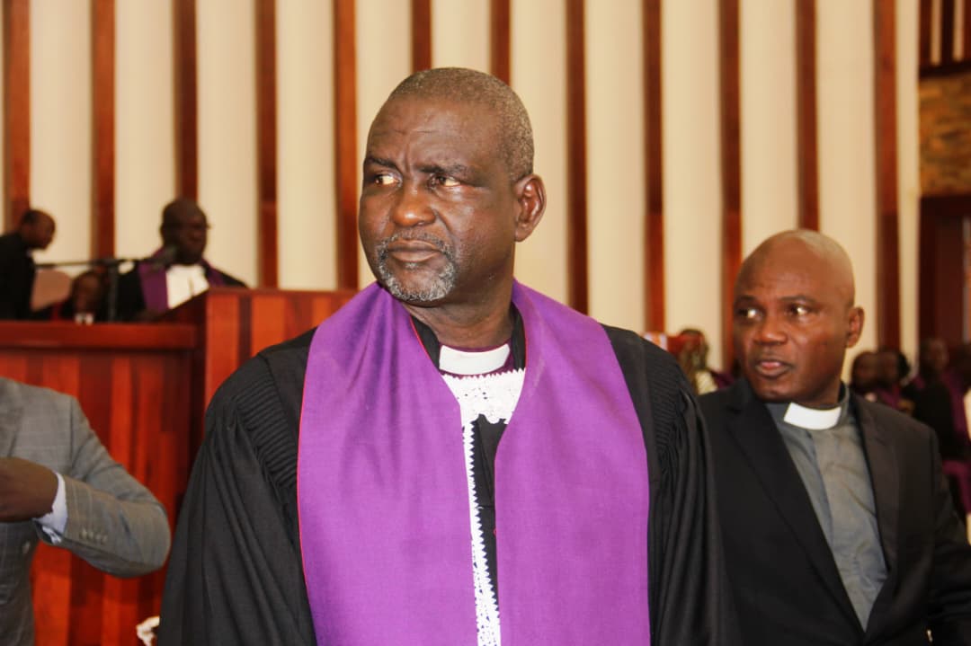 A pastor in a black gown and purple stole in a church sanctuary